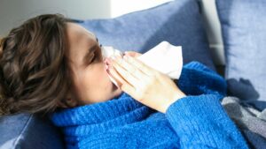 woman on couch blowing her nose sick with n1h1 showing swine flu symptoms