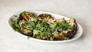 grilled aubergine on a white plate adorned with herbs and spices