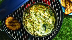 spinach and artichoke dip in a pot on a braai stand